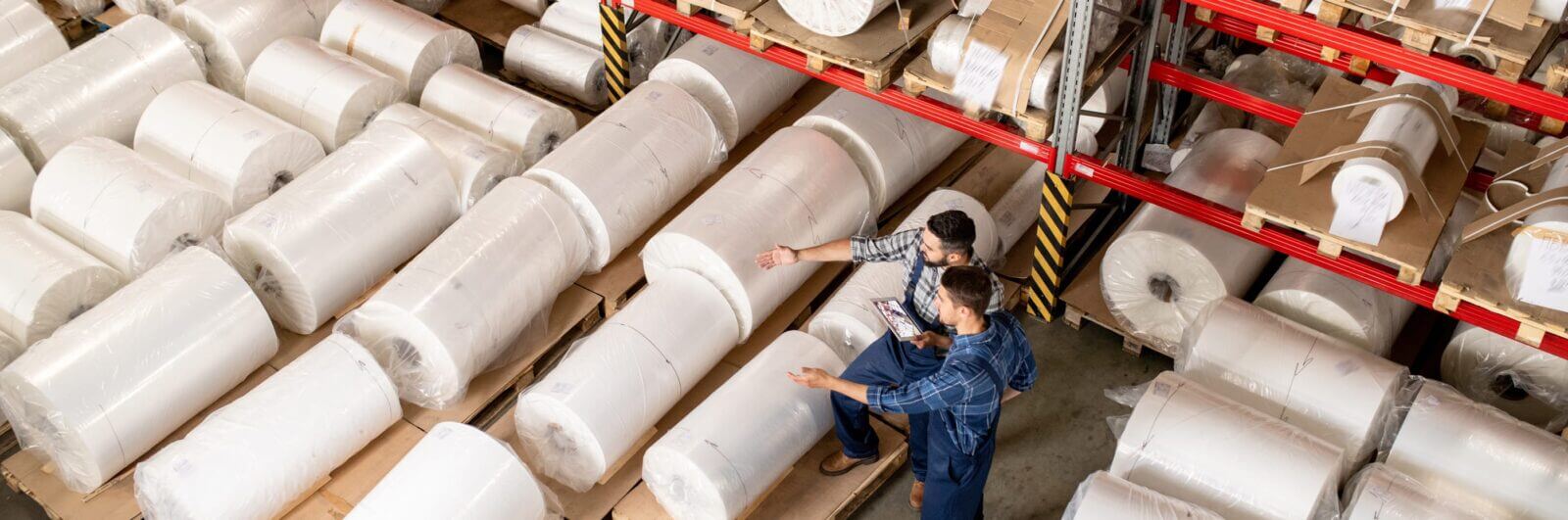 Workers examine huge rolls of paper at a paper warehouse